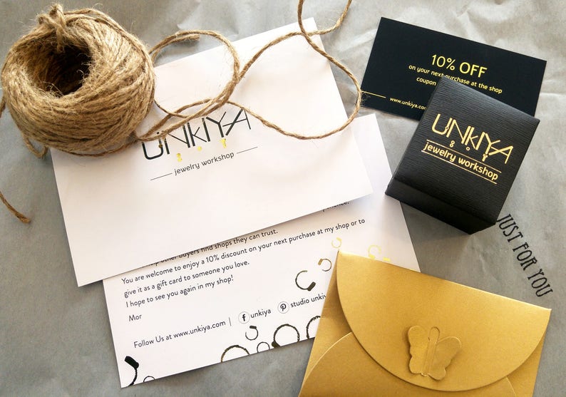 May include: A white card with the text "UNKIYA jewellery workshop" and a message about a 10% discount on the next purchase. A black box with the text "UNKINA jewellery workshop" and a gold envelope with a butterfly design.