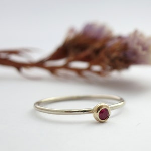 May include: A simple gold band ring with a small, round, red gemstone set in the centre.