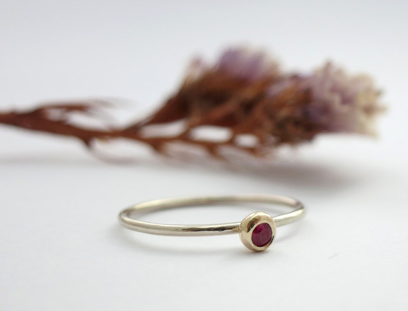 May include: A simple gold band ring with a small, round, red gemstone set in the centre.