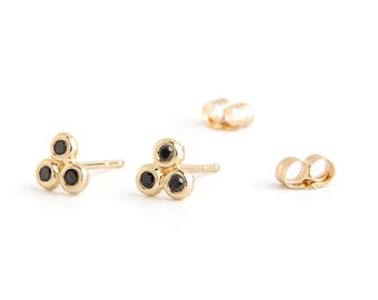 May include: A pair of gold earrings with three black gemstones arranged in a triangular shape.