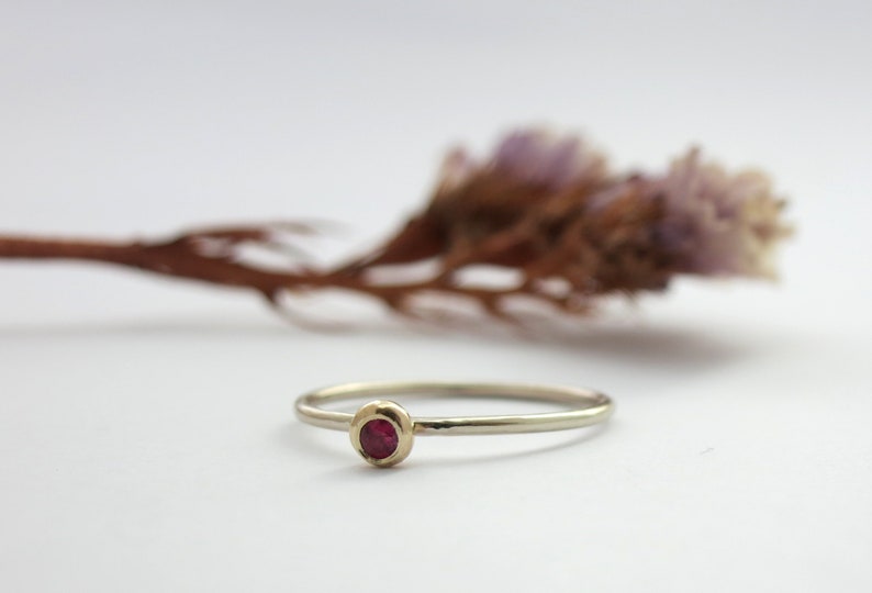 May include: A delicate gold ring with a single red gemstone set in the centre.