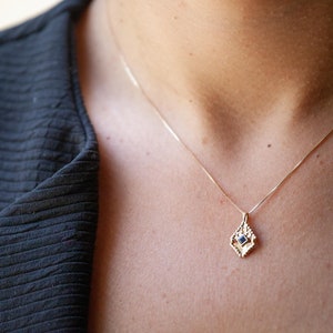 May include: A gold chain necklace with a delicate pendant featuring a small blue gemstone set in a geometric design.