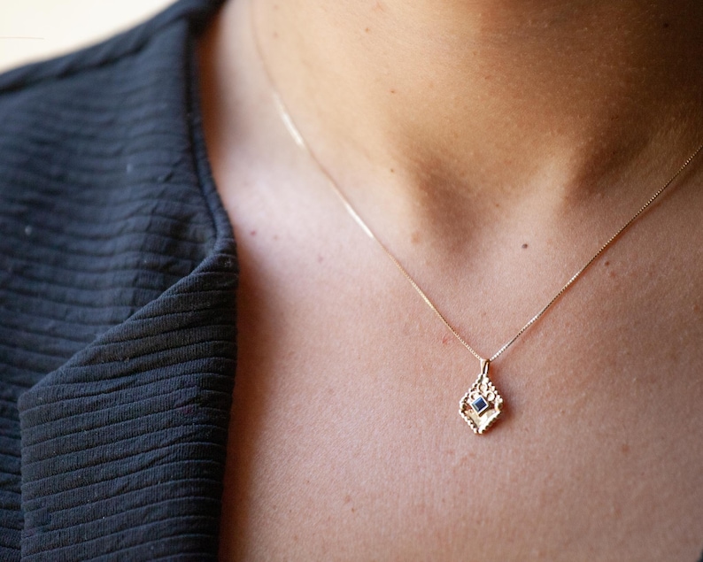 May include: A gold chain necklace with a delicate pendant featuring a small blue gemstone set in a geometric design.