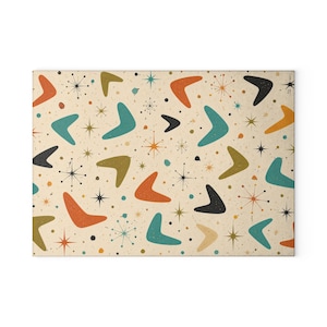 May include: A rectangular print featuring a repeating pattern of boomerang shapes in orange, teal, olive green, and black against a cream background. The design includes scattered starburst icons and small dots, creating a dense, multi-colored graphic composition.