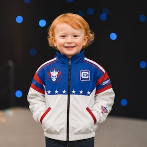 May include: A zip-up jacket featuring a color-blocked design in white, blue, and red. The chest displays a skull graphic with a crown and stars, a square logo with the letters CR, and the text CODY. White stars line the blue chest panel.