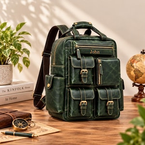 Puede incluir: Una mochila de cuero verde oscuro con múltiples bolsillos exteriores con hebillas y cremalleras en tono latón. La solapa frontal muestra el nombre John en letras doradas. Incluye correas de hombro marrones ajustables y un asa superior.