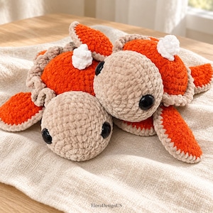 Può includere: Un peluche all'uncinetto raffigurante due tartarughe marine collegate con gusci arancioni vivaci e teste, pinne e ventri beige chiaro. Ogni tartaruga ha grandi occhi rotondi in plastica nera e un piccolo dettaglio bianco all'uncinetto sul guscio.