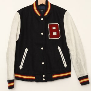 May include: A navy blue varsity jacket with white leather sleeves and a red felt letter "B" on the chest. The jacket has yellow and red striped ribbing at the collar, cuffs, and hem.