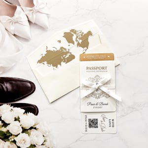 May include: A wedding invitation set featuring a passport-style booklet and a boarding pass with gold text. The envelope interior displays a gold world map. The invitation is tied with a white satin ribbon and includes the names Pinar and Burak.
