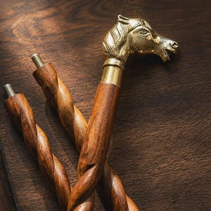 Puede incluir: Un mango de bastón con un remate de cabeza de caballo en latón pulido, unido a un eje de madera marrón oscuro con un diseño en espiral retorcido. El eje incluye un tornillo de metal roscado en la parte superior para su ensamblaje.