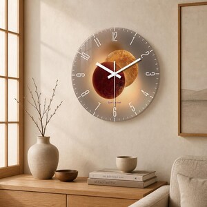 May include: A round wall clock featuring a celestial design with two overlapping planets in shades of deep red and golden yellow. The clock face has white Arabic numerals from 1 to 12 and white hour, minute, and second hands centered on the display.