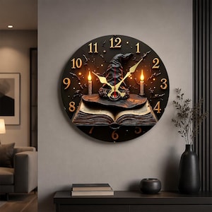 May include: A round black wall clock featuring a central illustration of an open book with a pointed hat resting on top, flanked by two lit candles. The clock face displays gold-colored numerals from 1 to 12 and thin gold clock hands.