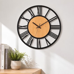 May include: A round wall clock featuring a black metal frame with large Roman numerals and a central circular light wood grain face. The clock has two black hands and a thin black second hand positioned in the center of the wooden dial.