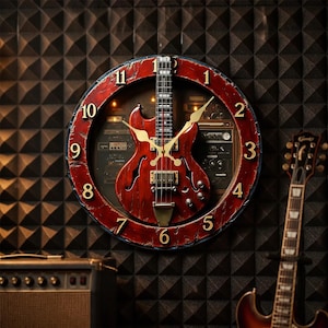 Pode incluir: Um relógio de parede circular com acabamento em vermelho desgastado e numerais dourados. O centro exibe um corpo de guitarra elétrica em miniatura integrado ao mostrador, sobre um fundo com imagem de equipamentos de áudio.