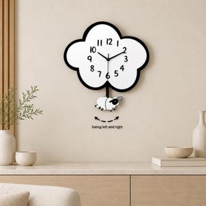 May include: A cloud-shaped wall clock with a white face, black border, and black numerals. A small white and black sheep pendulum hangs from the bottom, with text below reading Swing left and right and a dashed arrow indicating movement.
