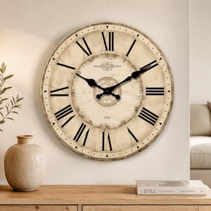 May include: A round wall clock with a cream-coloured face, black Roman numerals, and black spade-shaped hands. The centre features the text Marca Corona 1874 and Italy. The clock has a weathered, aged appearance with a dark circular border and minute markers.