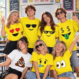 Peut inclure: Un groupe de personnes portant des t-shirts jaunes avec divers imprimés d'emojis, dont des yeux en cœur, des lunettes de soleil, des lunettes pixelisées et des signes dollar, et un t-shirt blanc avec un emoji caca marron, tous à manches courtes.