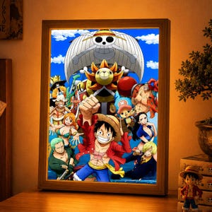 Peut inclure: Un caisson lumineux rectangulaire présentant une illustration animée vibrante de l'équipage de One Piece, avec Monkey D. Luffy au premier plan portant son chapeau de paille, entouré de ses compagnons et du navire Thousand Sunny sur un ciel bleu.