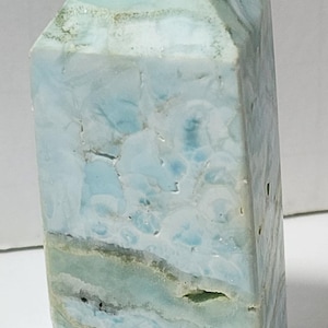 May include: A light blue, white, and green crystal point with a pointed top and a flat base. The crystal has a marbled appearance with swirls of color.