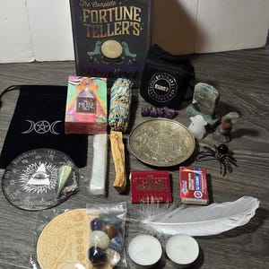 May include: An assortment of spiritual and divination tools, including a book titled "The Complete Fortune Teller's Handbook", tarot cards, crystals, a feather, candles, and a small black bag with the word "RUNES".
