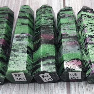 May include: Five green, black, and pink zultanite gemstone points, each with a hexagonal base. The points are labeled with the letters A, B, C, D, and E, followed by the number 14.