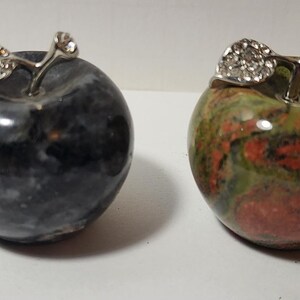 May include: Four small decorative apples made of different types of stone. The apples are green, black, red and brown. Each apple has a silver metal stem and leaf.