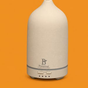 May include: A matte beige ceramic essential oil diffuser with a tapered teardrop shape. The base features two buttons labeled LIGHT and MIST, along with timer settings for 0H, 1H, 2H, and 4H. The logo B Beautirual Find Natural Rituals of Beauty is printed.