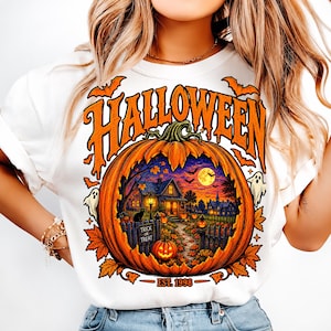 Könnte beinhalten: Ein weißes T-Shirt mit einer großen orangefarbenen Kürbisgrafik und dem Wort HALLOWEEN in orangefarbenen Buchstaben darüber. Der Kürbis enthält eine Szene mit einem Haus, einer schwarzen Katze, Geistern und Fledermäusen. Der Text EST. 1998 steht darunter.