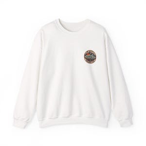 May include: A white long-sleeve crewneck sweatshirt featuring a circular graphic on the left chest. The graphic depicts a flat earth illustration with the text "FLAT EARTH RESEARCH TEAM" in a dark red border, including a small sun and moon.