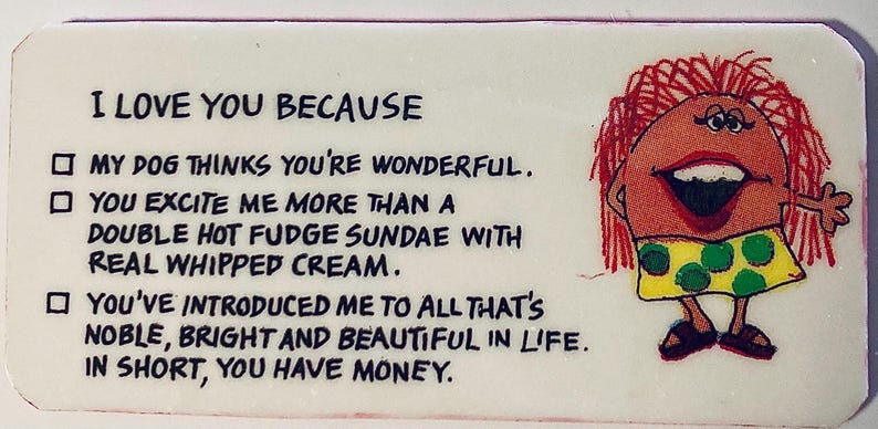May include: A rectangular, white novelty item with the text "I LOVE YOU BECAUSE" and humorous reasons. A cartoon figure with red hair and a yellow dress with green polka dots is on the right.