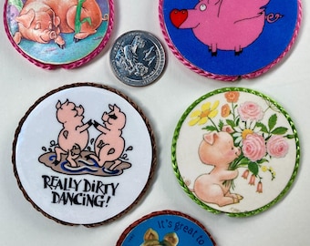 May include: Five round embroidered patches featuring pigs. One patch shows a pink pig sleeping next to corn. Another patch shows a pink pig flying with wings. A third patch shows two pink pigs dancing in mud with the text "Really Dirty Dancing!" A fourth patch shows a pink pig holding a bouquet of flowers. The last patch shows Miss Piggy from the Muppets with the text "It's great to be Moi!"