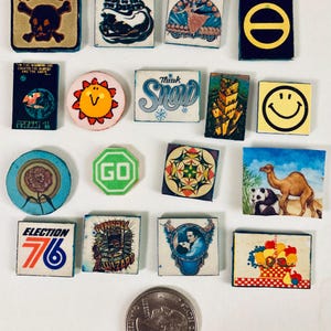 May include: A selection of vintage square and circular pins with diverse designs. The pins display images of a skull and crossbones, a smiling sun, the word "Snow", a camel and panda, and the text "Election 76".