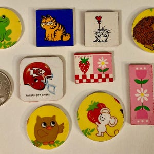 May include: A collection of nine colorful ceramic tiles with various designs. The tiles feature a green frog, a cartoon cat, a cat with a heart balloon, a hedgehog, a football helmet, a strawberry and flower, a flower and stem, an owl, and a mouse with a strawberry.