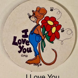 May include: A round, off-white button with a cartoon mouse wearing blue overalls and holding red flowers with yellow centers. The text "I Love You" is in purple, with two small bees and a dotted line design.