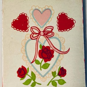 May include: A vintage greeting card with a white background featuring red hearts, roses, and a pink bow. The card has a light blue heart outline with a pink heart inside. Green leaves and stems accent the roses.