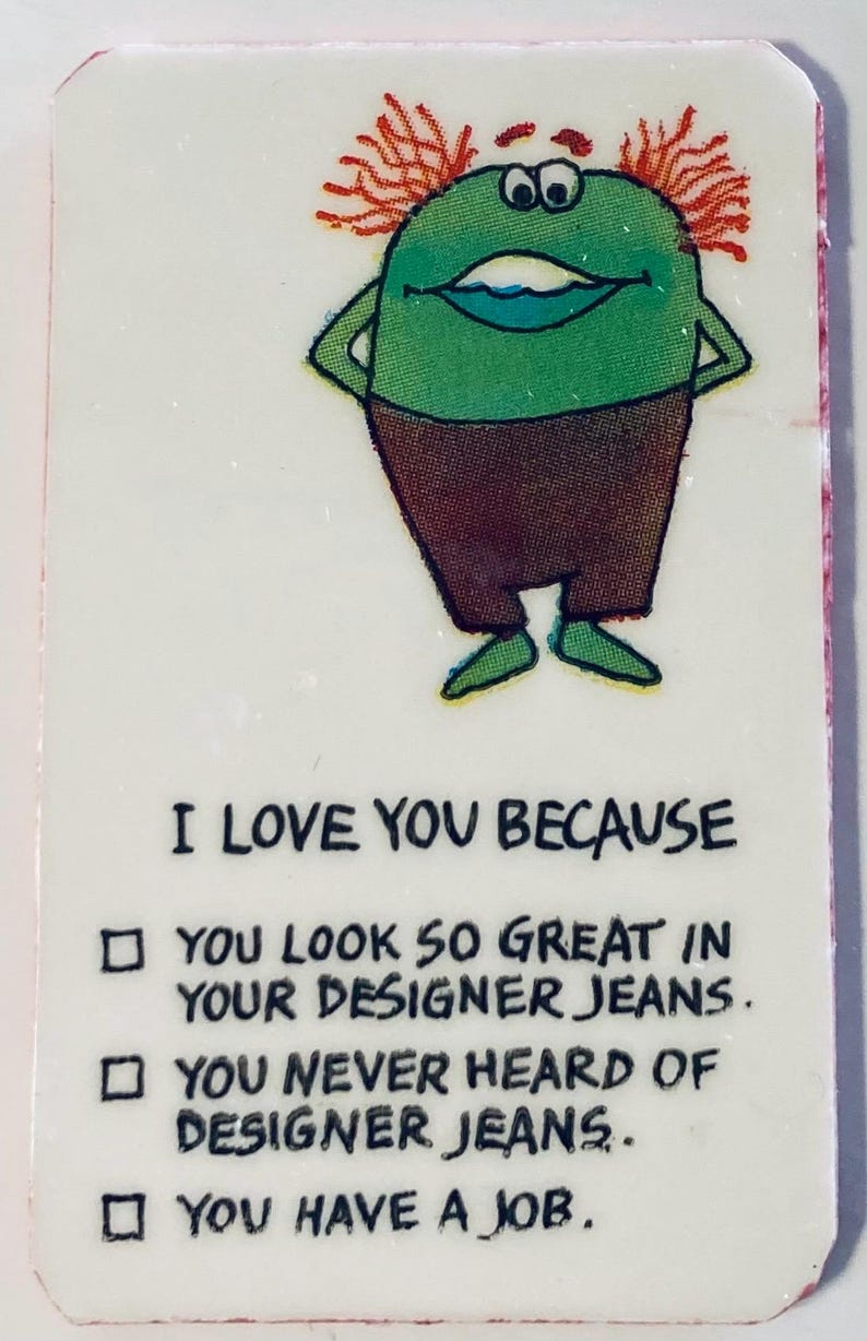 May include: A rectangular card with a cartoon character and text. The green character has orange hair and brown pants. Text reads: "I LOVE YOU BECAUSE...YOU LOOK SO GREAT IN YOUR DESIGNER JEANS...YOU NEVER HEARD OF DESIGNER JEANS...YOU HAVE A JOB."