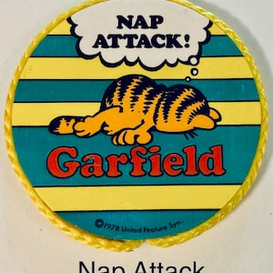 Pu&ograve; includere: Una toppa rotonda di Garfield con bordo giallo. La toppa raffigura Garfield che dorme, con le parole "NAP ATTACK!" in un fumetto. La parola "Garfield" &egrave; rossa e lo sfondo ha strisce gialle e turchesi.