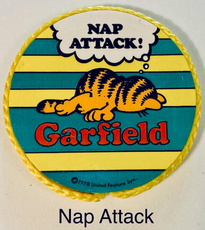 Pu&ograve; includere: Una toppa rotonda di Garfield con bordo giallo. La toppa raffigura Garfield che dorme, con le parole "NAP ATTACK!" in un fumetto. La parola "Garfield" &egrave; rossa e lo sfondo ha strisce gialle e turchesi.