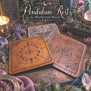May include: Two square leather pendulum rests featuring intricate laser-engraved designs. One tan rest displays a lunar cycle and celestial motifs, while the other brown rest features a geometric star compass pattern with botanical accents and stitching.