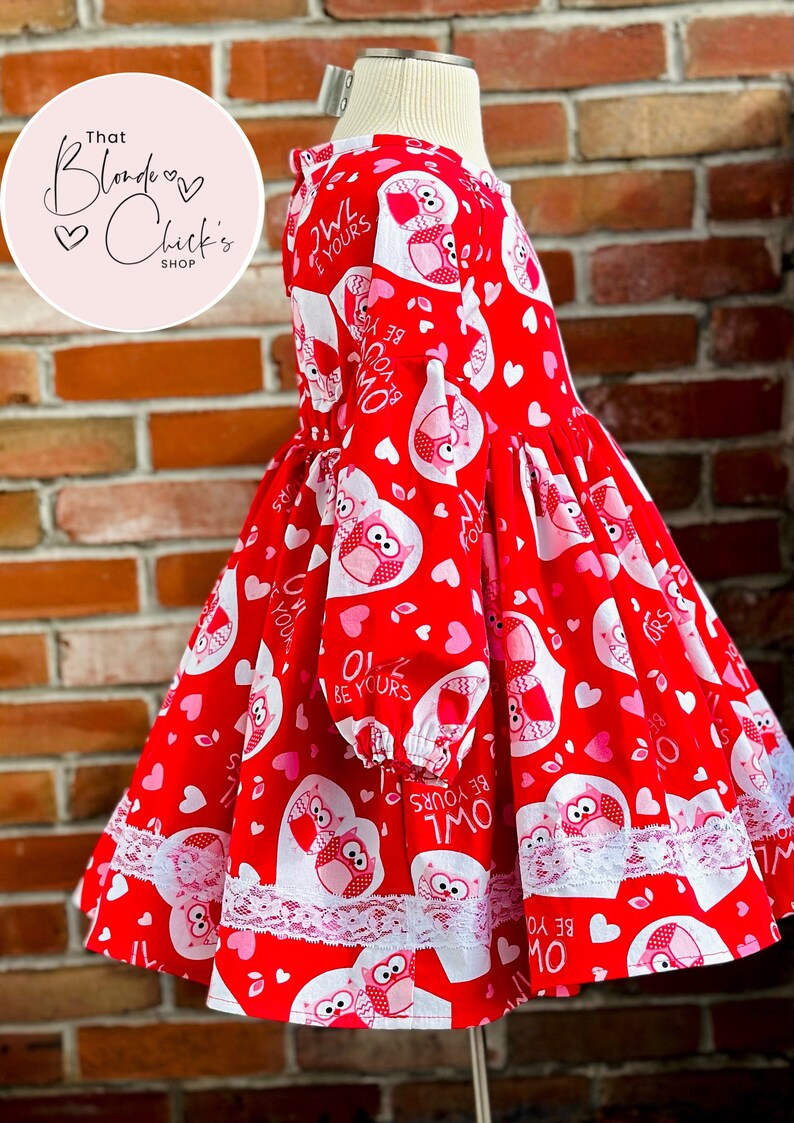 May include: Red and white dress with a Valentine's Day owl print. The dress has long sleeves and a white lace trim. The dress has the text "Owl Be Yours" repeated on the fabric.