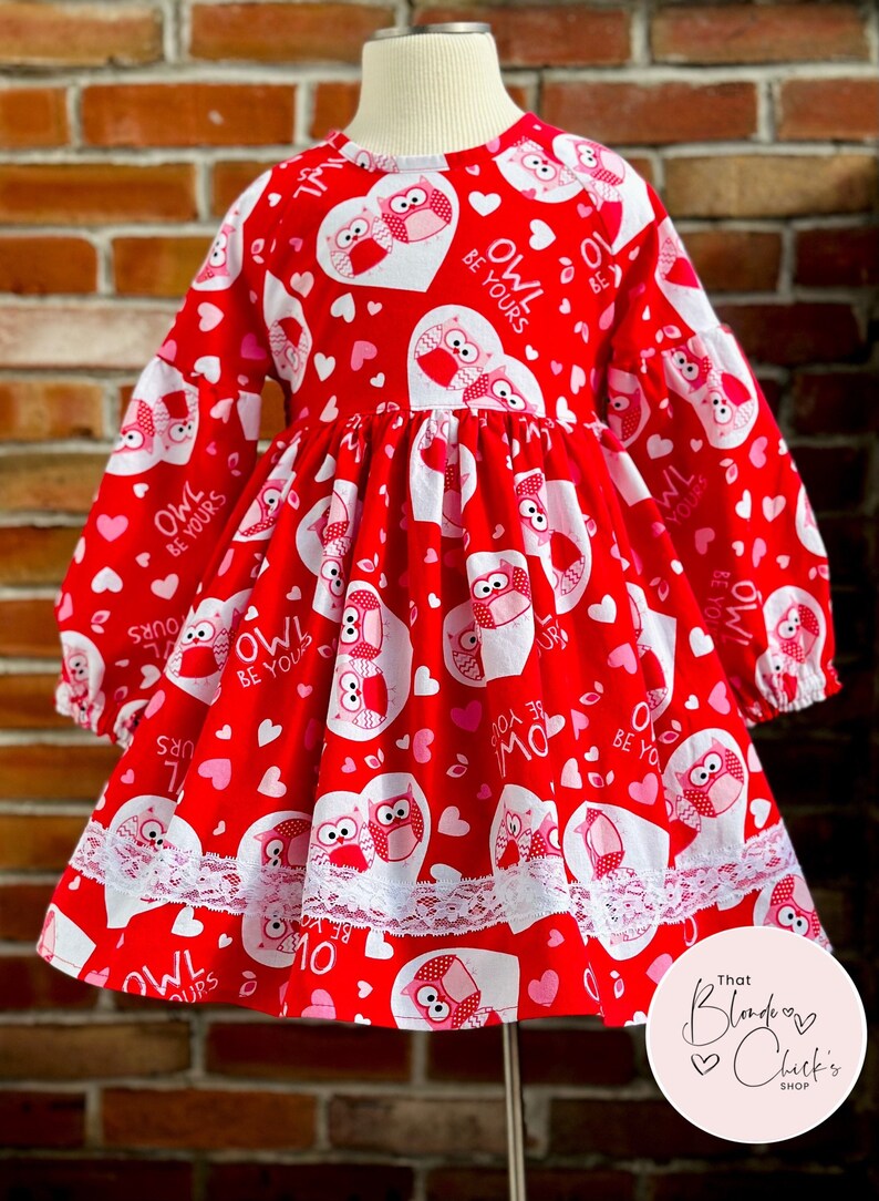 May include: Red dress with long sleeves and a white lace trim. The dress has a pattern of pink hearts and owls with the text "Owl Be Yours".