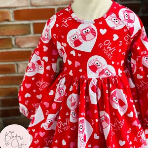 May include: Red long-sleeved dress with a white lace trim. The dress features a heart and owl pattern with the text "Owl Be Yours".