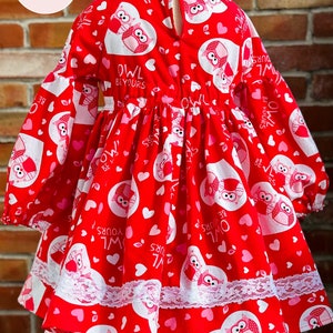 May include: Red dress with long sleeves and a white lace trim. The dress has a pattern of pink hearts and owls with the text "Owl Be Yours".