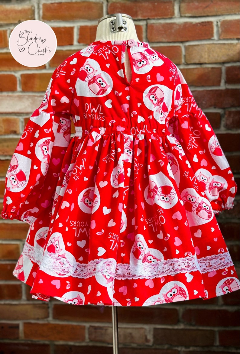 May include: Red dress with long sleeves and a white lace trim. The dress has a pattern of pink hearts and owls with the text "Owl Be Yours".