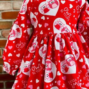 May include: Red and pink Valentine's Day dress with a white heart pattern and owls. The dress has a lace trim and says "Owl Be Yours" on the hearts.