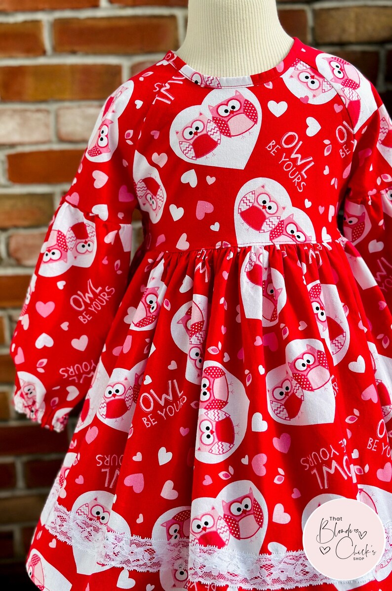 May include: Red and pink Valentine's Day dress with a white heart pattern and owls. The dress has a lace trim and says "Owl Be Yours" on the hearts.