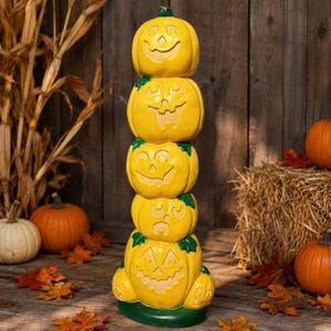 Può includere: Una pila verticale di cinque zucche gialle con volti intagliati, dotate di piccioli verdi e una base verde. Ogni zucca mostra un'espressione unica, inclusi volti sorridenti, che fanno l'occhiolino e con espressioni di sorpresa.