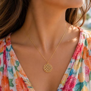 May include: A gold-toned necklace featuring a circular pendant with an intricate, openwork geometric pattern resembling a flower of life design. The pendant hangs from a delicate, thin gold-toned chain that rests against the collarbone area.