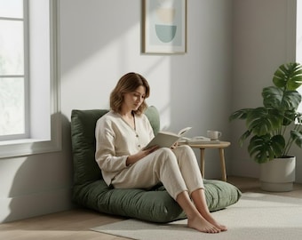 Puede incluir: Un sillón de suelo tapizado en tela verde oliva oscuro con asiento y respaldo acolchados y capitoné. El sillón presenta un diseño de perfil bajo que se apoya directamente en el suelo, proporcionando una superficie suave y acolchada.