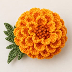 May include: A crocheted marigold flower with vibrant orange layered petals and a textured dark orange center. The flower is attached to a stem with three detailed green leaves, all crafted with intricate yarn stitching techniques.